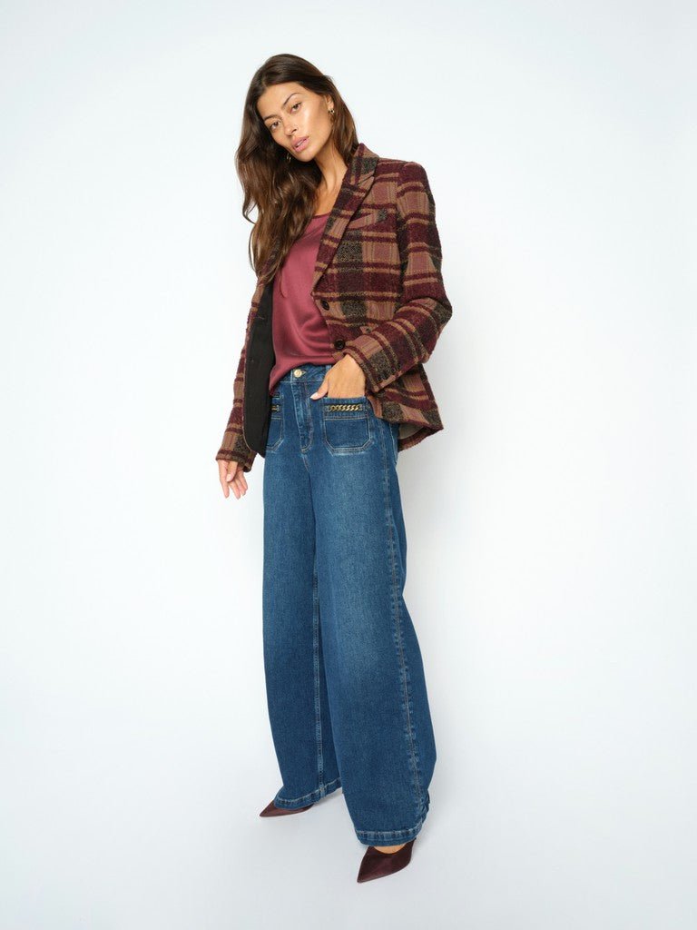 En kvinde iført en ternet blazer, en bordeauxrød top, MOS MOSH Colette Denim-jeans og brune sko står foran en ensfarvet baggrund.