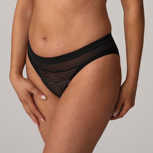 Model iført PrimaDonnas Sophora Black Sort-lingeri med højt skåret ben, hånden på låret, foran en ensfarvet baggrund.