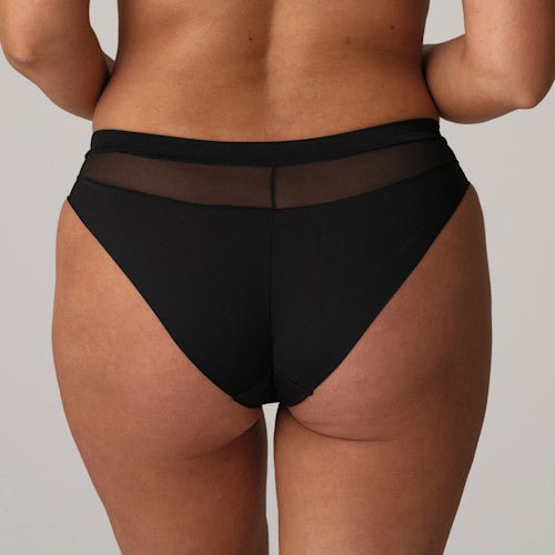 Model iført PrimaDonna Sophora Black-trusser med netdetaljer og høj udskæring, fotograferet bagfra på en neutral baggrund.