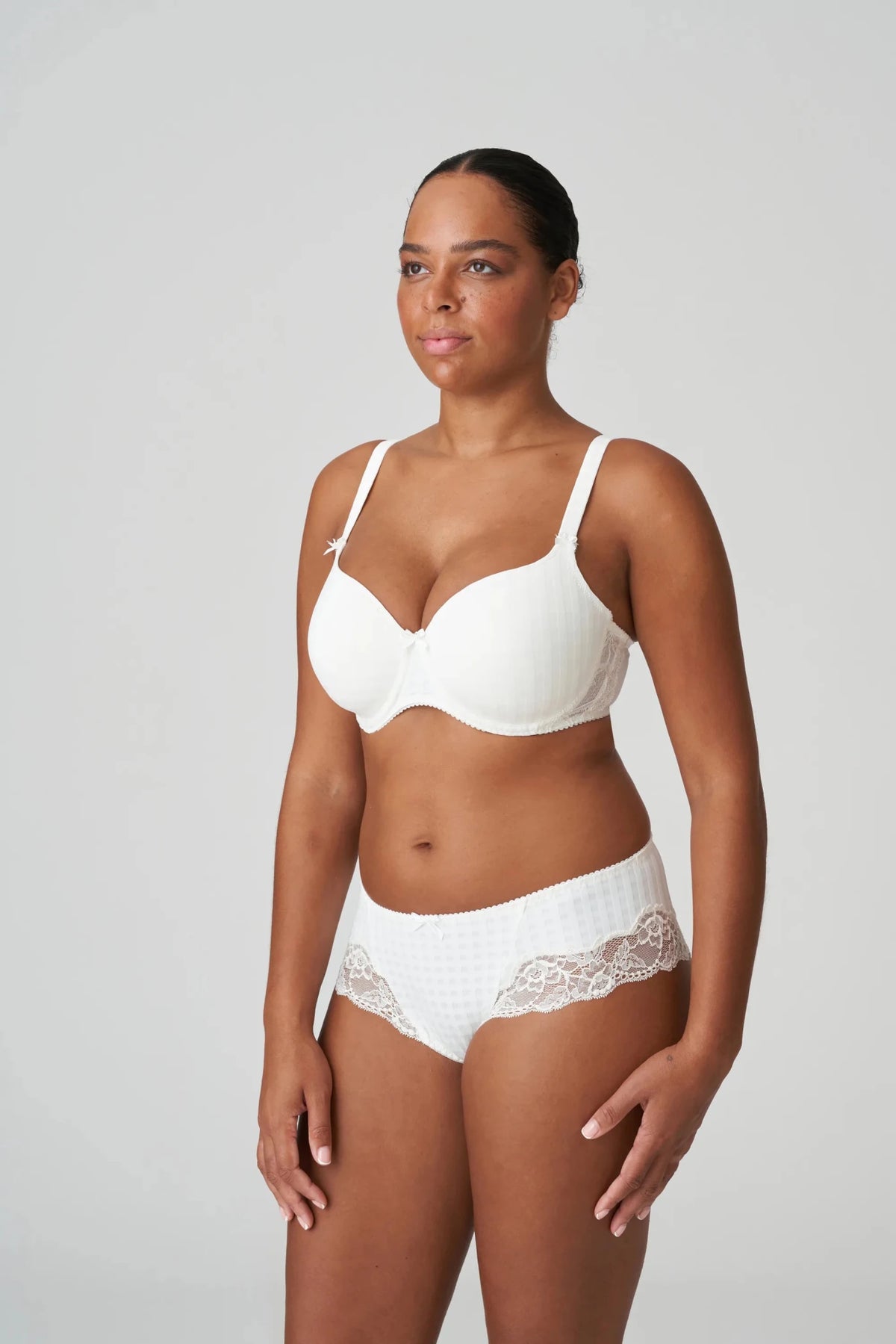Kvinde iført en PrimaDonna Madison Natur off-white-bh og hipster, stående foran en ensfarvet lysegrå baggrund.