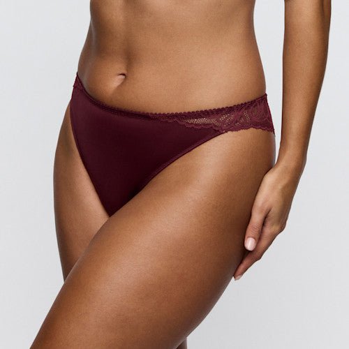 Modellen bærer PrimaDonna 155416 G-streng i farven Evening Red Bordeaux, fotograferet fra maven til låret foran en ensfarvet baggrund.