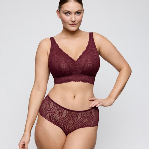 Modellen bærer et sæt bestående af en G-streng og en bh fra PrimaDonna, model 155417, i farven Evening Red Bordeaux, og poserer foran en lysegrå baggrund.