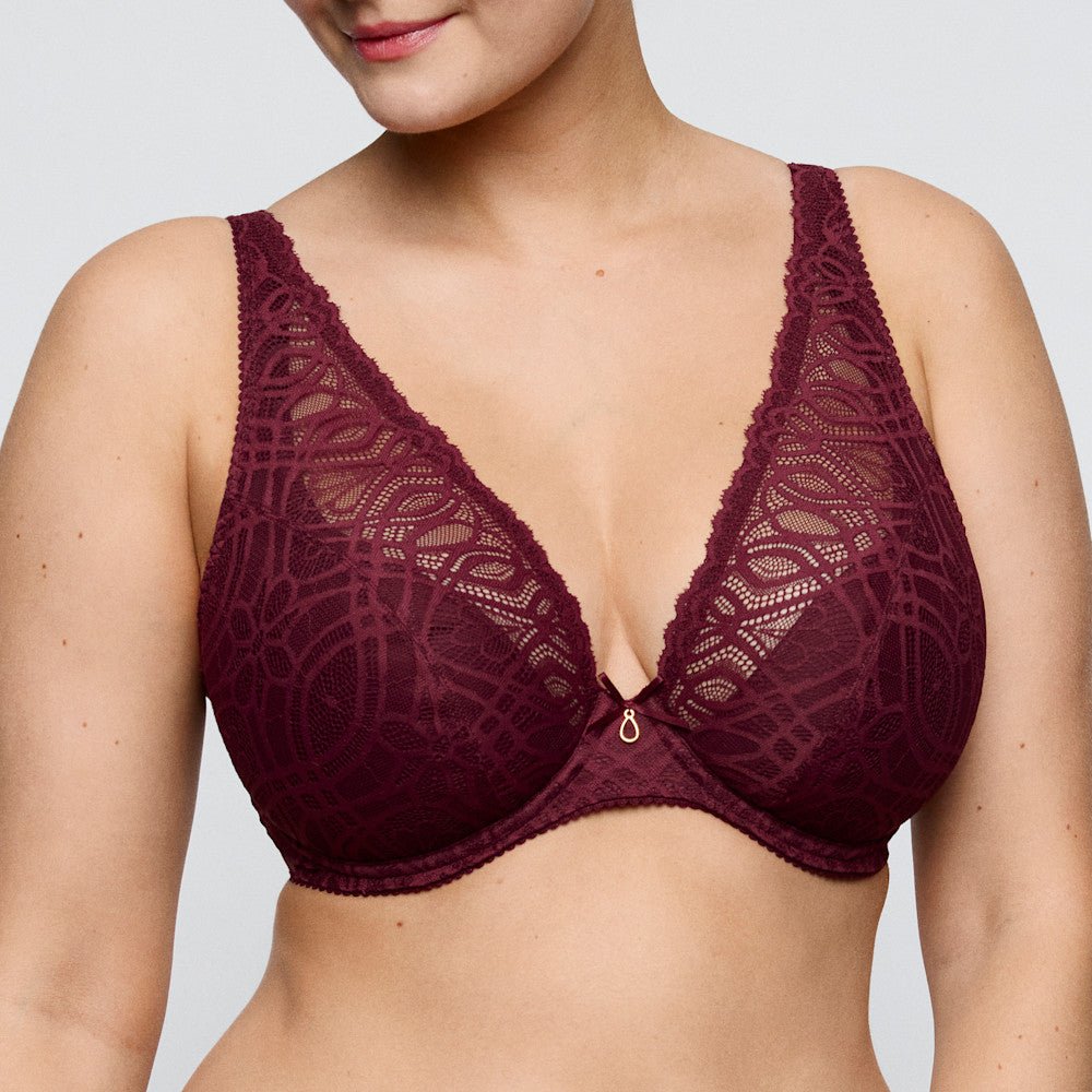 Kvinden bærer en PrimaDonna 155421-bh i farven Evening Red Bordeaux med geometrisk blonder og et dekorativt vedhæng i midten.