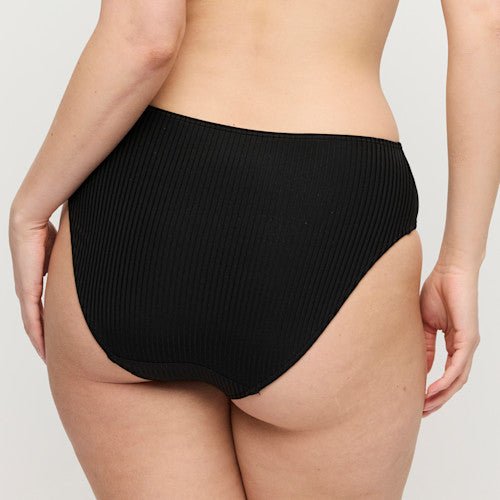 Modellen bærer PrimaDonna Swim – Delray Black Sort 155256, en bikiniunderdel med høj talje og ribstrik, foran en ensfarvet baggrund.