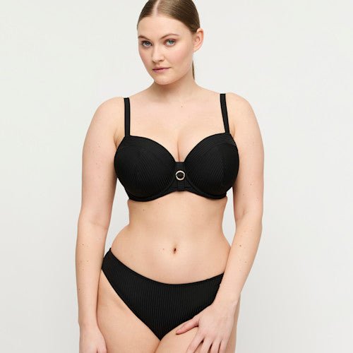 Kvinde i PrimaDonna Swim – Delray Black Sort bikinitop, der står med ansigtet fremad foran en lys baggrund.