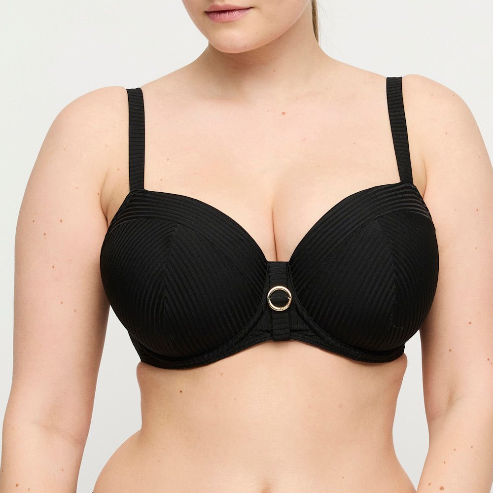 En kvinde har en PrimaDonna 155257 Delray Black-bikinitop på med tynde stropper og en dekorativ ring i midten.
