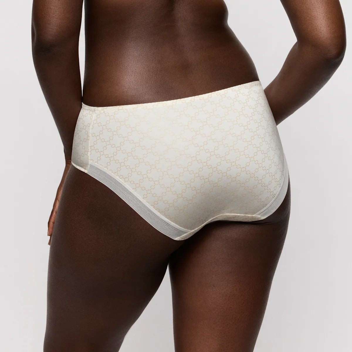 En person iført PrimaDonna Twist Kero Natural Off White maxi-trusse, set bagfra mod en ensfarvet baggrund.