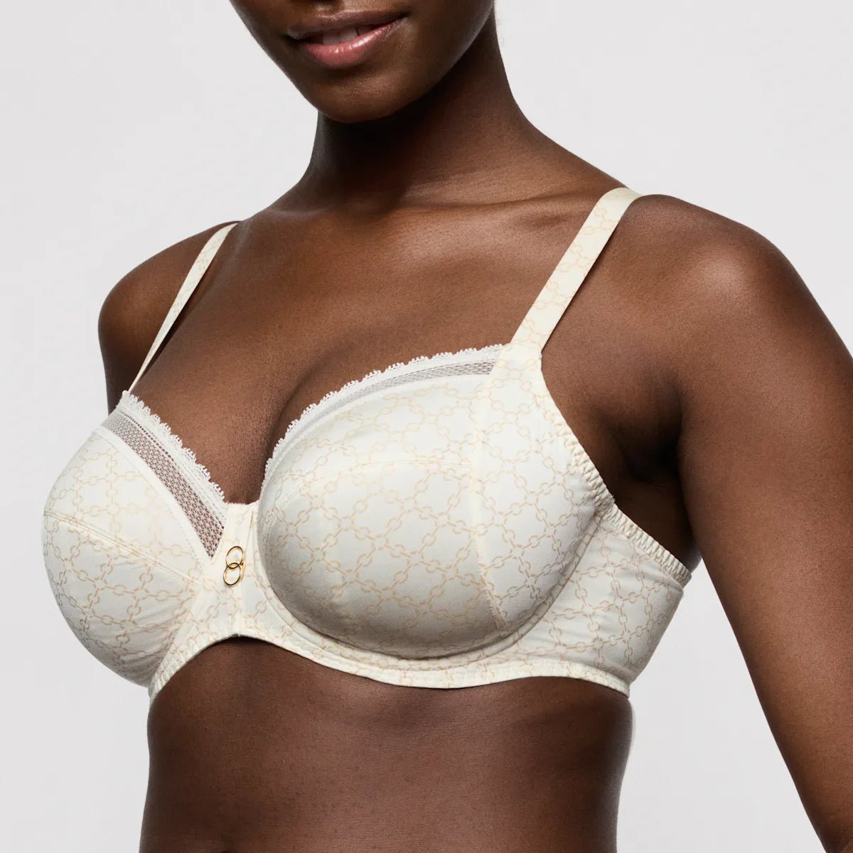 Model iført PrimaDonna Twist 154602 Kero Natural cremefarvet bh med bøjle, blondekant, blonder, gulddetaljer og grafisk mønster.