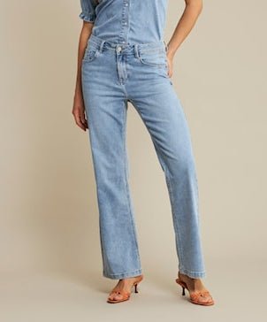 En person har Red Button Colette L33-jeans i lys denim, en denimskjorte og brune sandaler med hæl på og står foran en beige baggrund.