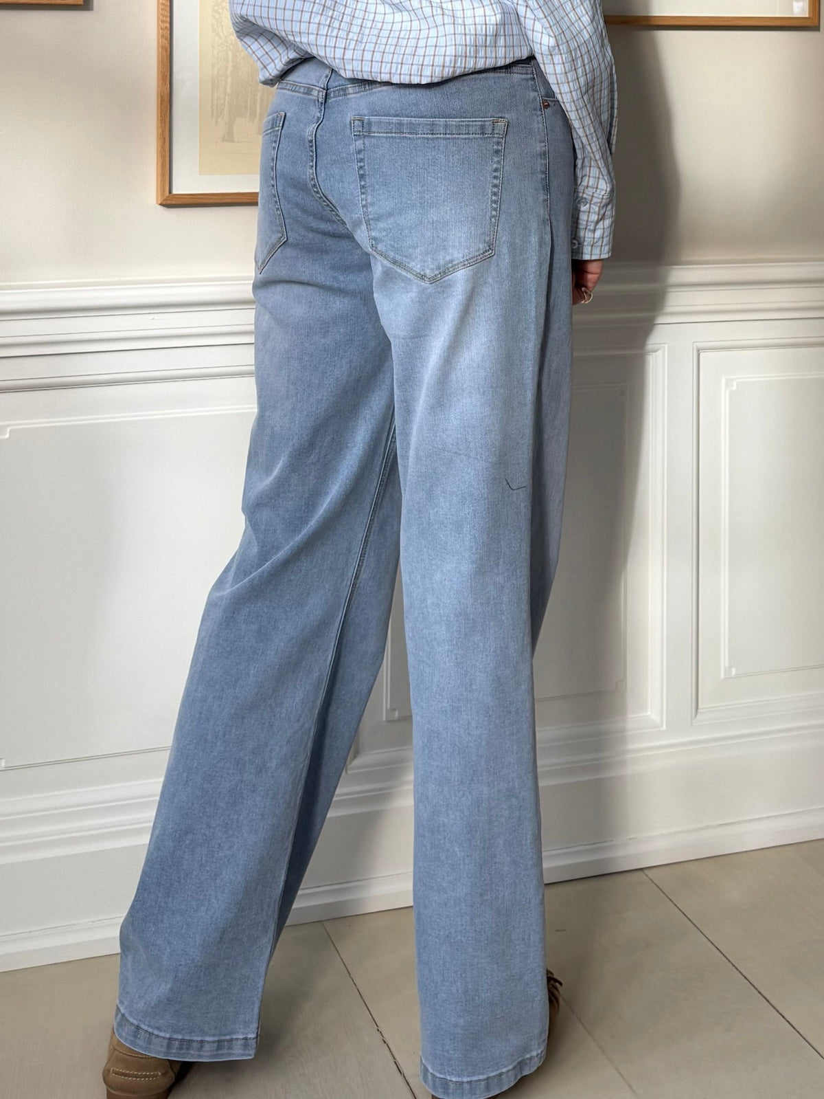 En person iført Red Button Colette L33 Lys-jeans og en ternet skjorte står indendørs med ryggen til kameraet.