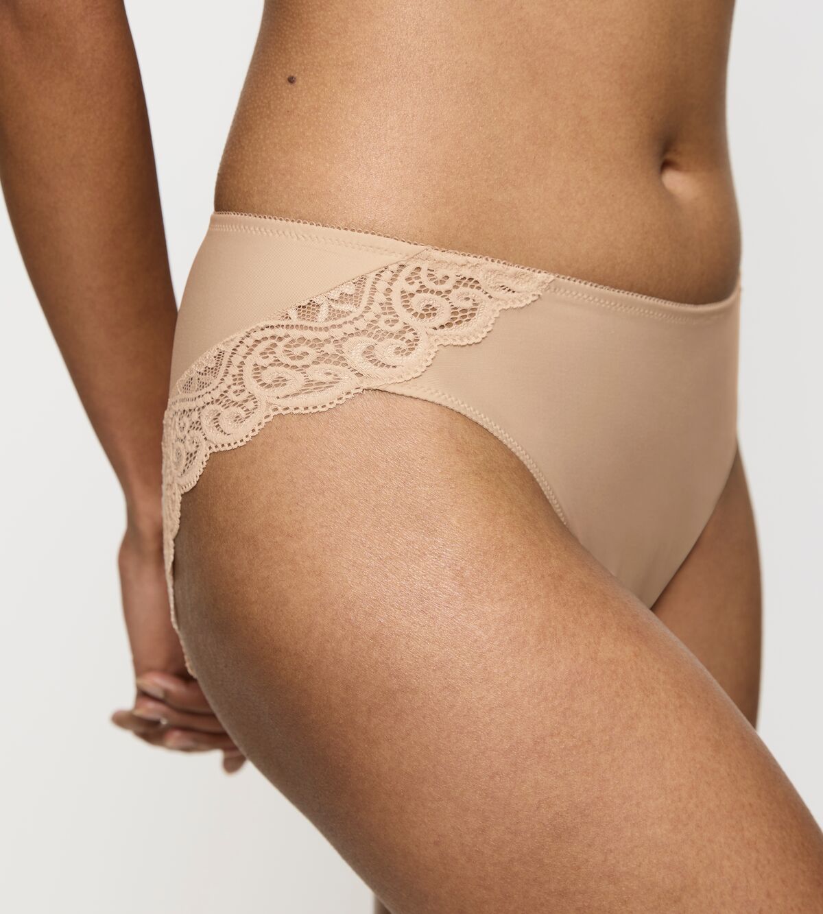 Modellen bærer Triumph Amourette 0026 Pudder-undertøj med blonder, set fra taljen til låret foran en ensfarvet baggrund.
