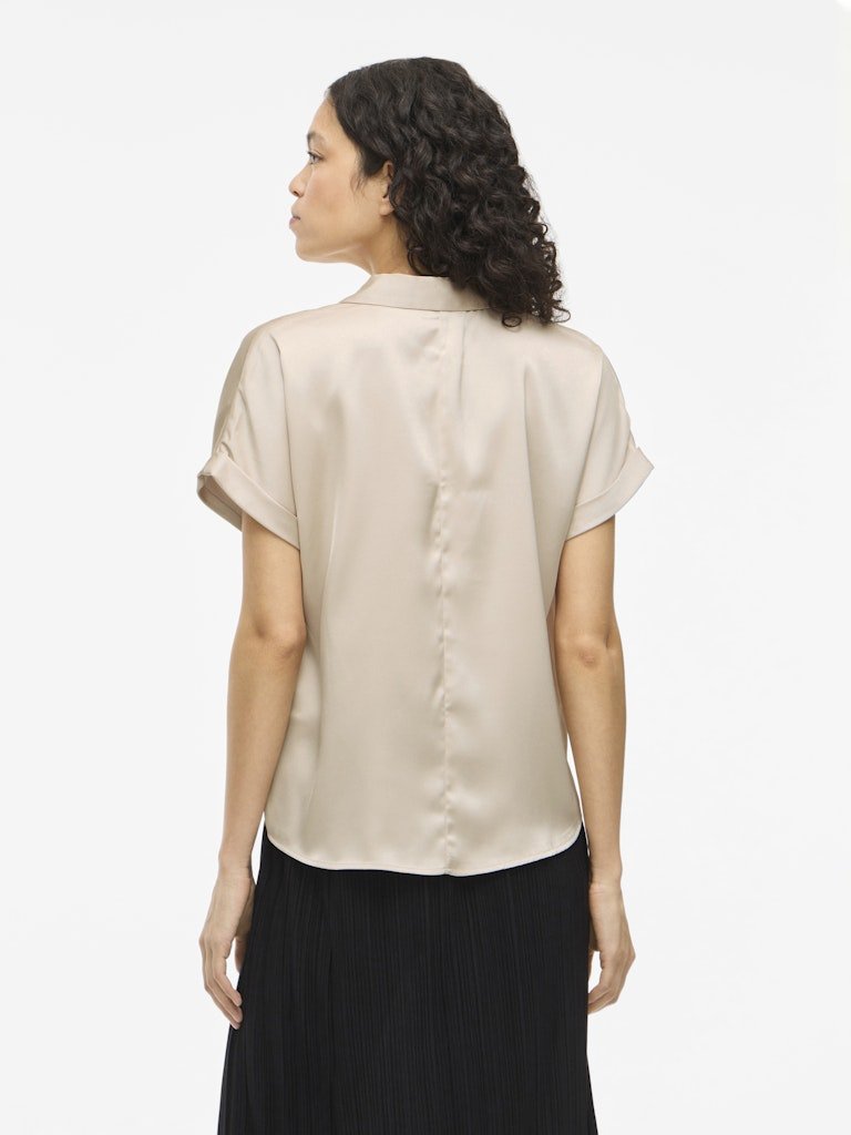 Kvinde med krøllet hår iført en VILA Vienna Ravenna Beige-top, set bagfra på en ensfarvet baggrund.