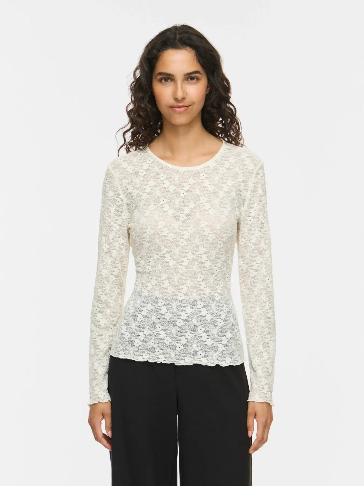 En kvinde iført en offwhite Fay-bluse fra VILA, der står foran en hvid baggrund.