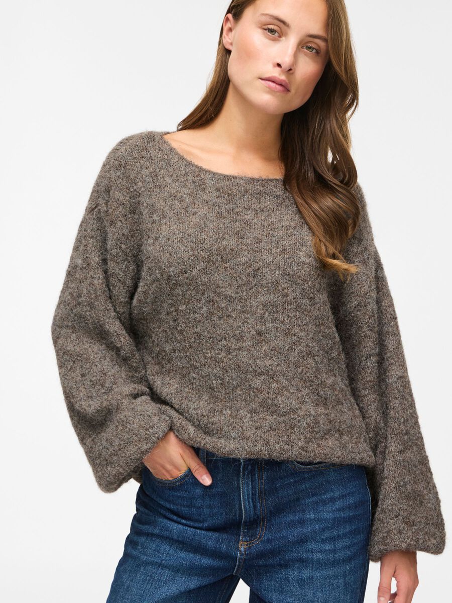 En kvinde er iført en brunmeleret bluse fra VILA Vimarley og blå jeans, med den ene hånd i lommen, foran en ensfarvet baggrund.