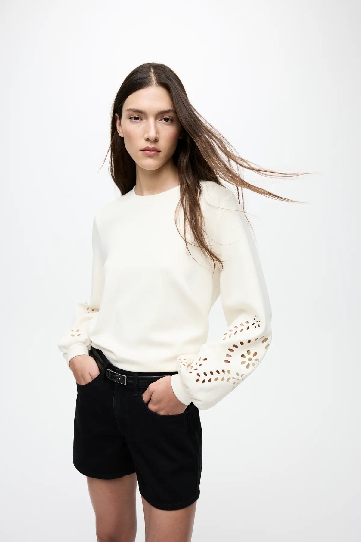 En kvinde står med hænderne i lommerne iført en VILA Visandy Off White-sweatshirt 155329 og sorte shorts.