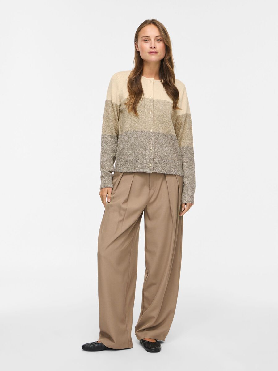 En kvinde har en VILA VISposa-cardigan i farvekombination creme/beige/grå og bukser med brede ben på.
