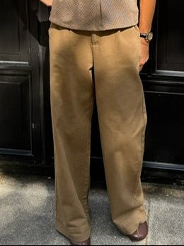 En person udendørs iført WithBlack – Steffi Camel-bukser, brune sko og et ur – perfekt til et stilfuldt look med brede ben.