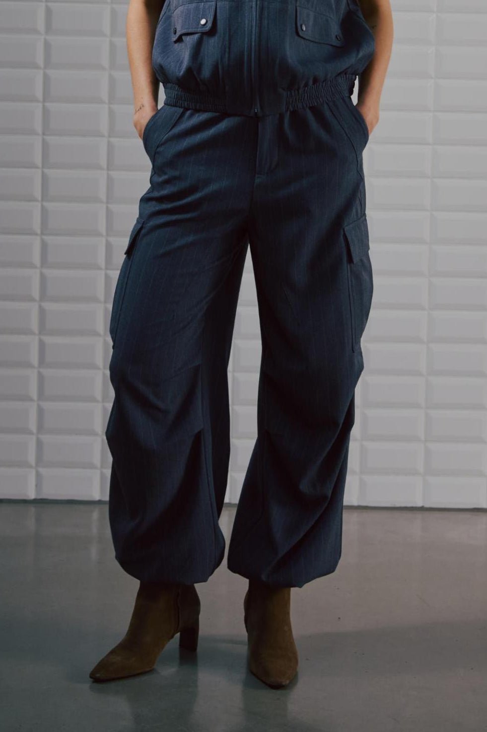 En person iført en 156398 | WithBlack – Anna Mørkeblå mørkeblå, bredbenet jumpsuit med fine striber, cargolommer og støvler.