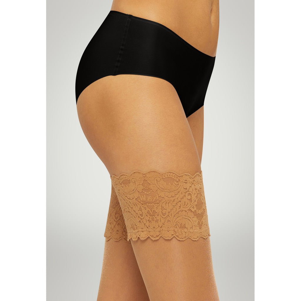Modellen bærer Wolford – Satin Touch 20 Gobi og sidder foran en neutral baggrund med farveovergange.