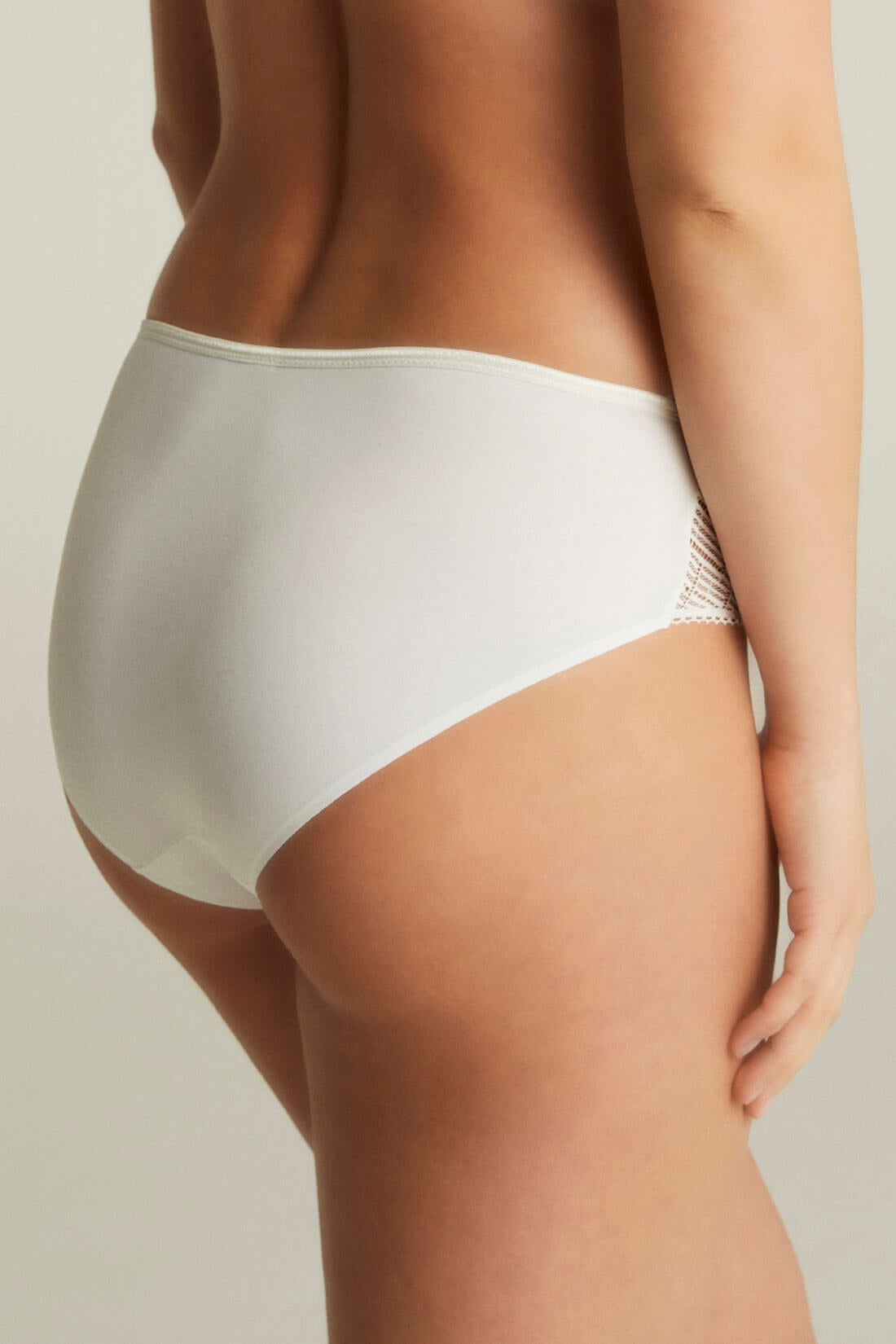 Model iført Chantelle EasyFeel Emma Milk-undertøj i off-white med blonder på ryggen, foran en neutral baggrund.