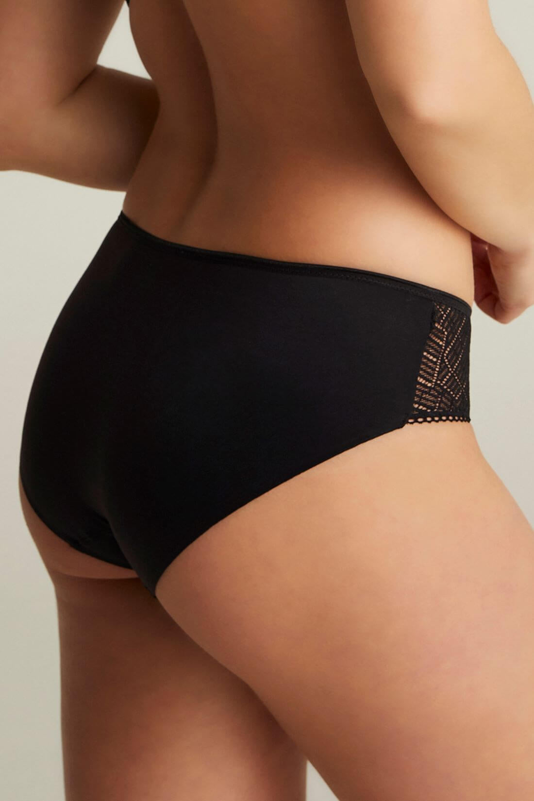 Modellen bærer Chantelle EasyFeel – Emma Black Sort, vist set bagfra med blonde-detaljer på en neutral baggrund.