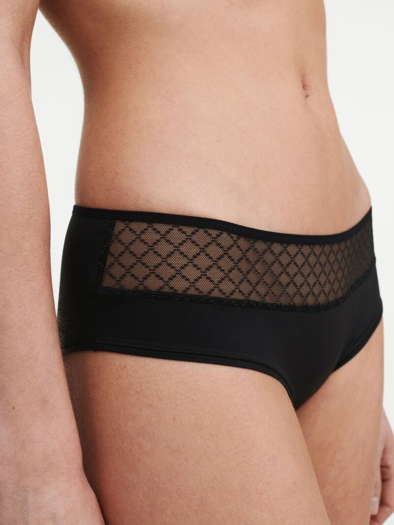Model iført Chantelle EasyFeel Norah Chic 011 Sort hipster med gennemsigtig, mønstret mesh-detalje i taljen, set fra siden.