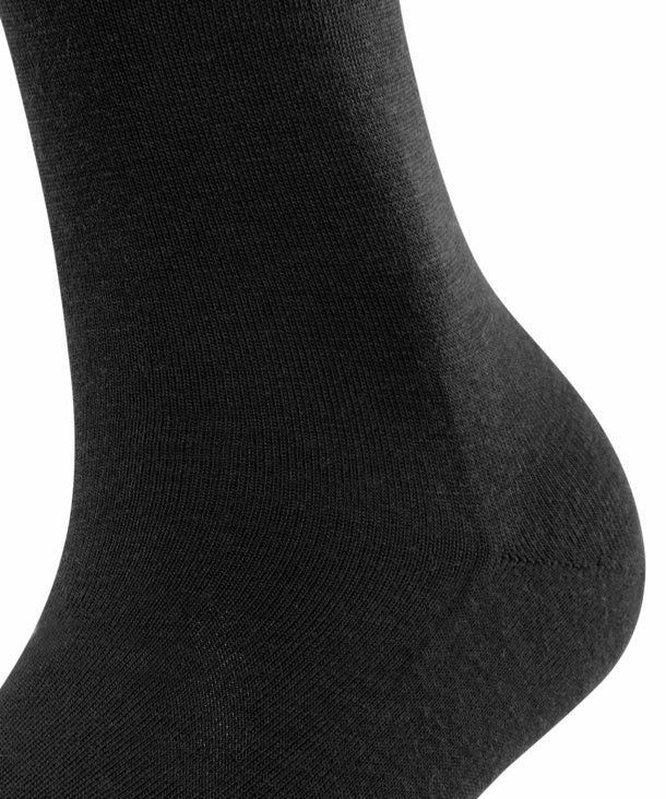 Nærbillede af Falke Softmerino SO Black F knæstrømper på en fod mod en hvid baggrund, der giver et klassisk look.